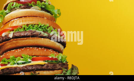 Riesige leckere frische Burger als Cak auf gelben Hintergrund. Cheeseburger mit Fleisch Schnitzel, Gemüse, Käse, Salat und Sauce. Fastfood, ungesunde f Stockfoto