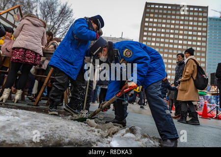 Öffentliche Beamte gefrorener Schnee schaufeln in Odori Park, Central Sapporo. Hokkaido, Japan. Stockfoto