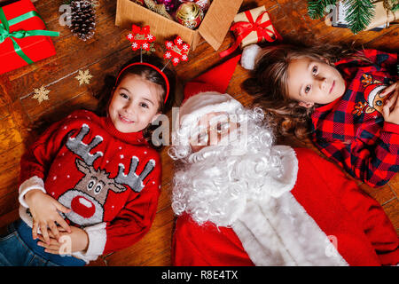 Zwei Mädchen und Santa liegen auf dem Boden zu Hause in der Nähe von Weihnachten Baum Stockfoto