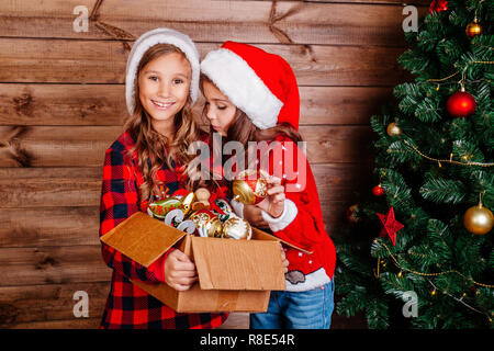 Frohe Weihnachten und schöne Feiertage. Süße kleine Schwestern schmücken den Baum zu Hause. Stockfoto