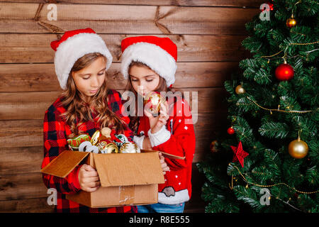 Frohe Weihnachten und schöne Feiertage. Süße kleine Schwestern schmücken den Baum zu Hause. Stockfoto