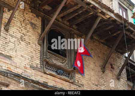 Nepalesische Flagge aufhängen außerhalb einer Holz Fenster in Patan, Kathmandu, Nepal geschnitzt. Stockfoto