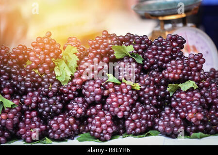 Frische rote Traube/Stapel der reife rote Traube auf die Trauben und Blätter auf dem Markt - lila Traube für Verkauf Essen inländischen Skala Hintergrund Stockfoto