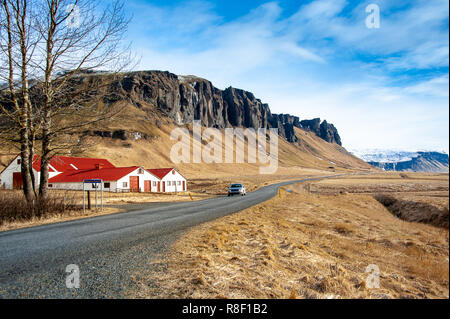 Ringstraße Nr. 1, in der Nähe von Skeidararsandur, südlichen Island. Malerische Szene, rote überdachte Bauernhäuser, schneebedeckte Gebirge, langer Weg vor uns. Stockfoto