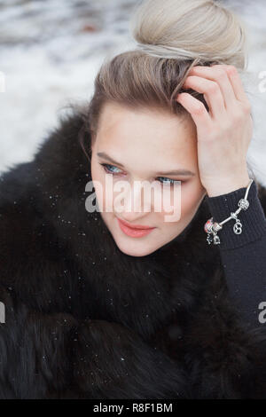 Closeup Portrait Mädchen sitzt auf einem Schnee in der City am Bordstein mit Schnee bedeckt. Lifestyle. winter Stimmung, Kaffeetasse, Mink Pelze Kleidung. Stockfoto