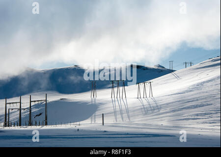 Wasserkraft Linien an Krafla Geothermie-kraftwerk, Island. Die untergehende Sonne wirft lange Schatten über verschneite Berglandschaft. Stockfoto