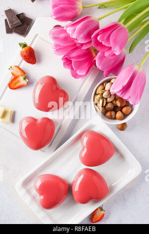 Rote herzförmige Mousse Kuchen mit Beeren und Schokolade. Stockfoto