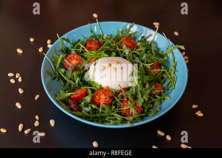 Burrata Käse Salat mit Tomaten, Rucola und Zahnräder. Auf einem blauen Schild und ein Schwarzer Tisch. Stockfoto