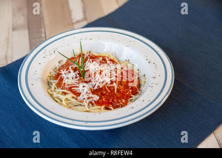 Luftbild des weißen Teller Spaghetti Bolognese mit Tomaten Sauce, Fleisch und Käse in einem blauen Tischdecke auf einen hölzernen Tisch bereit zu essen Stockfoto