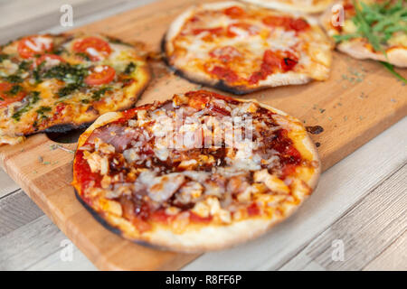 Nahaufnahme von einem Grill Pizza mit Speck, Hähnchen, Käse und Sauce auf einem Holzbrett auf einem Holztisch Stockfoto