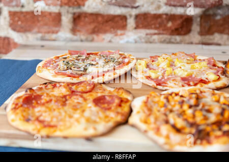 Vier kleine Pizzen auf einem Holzbrett, frisch aus dem Ofen, bereit, im Restaurant zu essen. Fokus auf carbonara Pizza. Auf einem Holztisch mit einem blauen Tabl Stockfoto