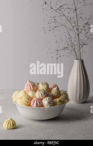 Süße Marshmallow in der Tasse, leckeres Dessert, auf einem grauen Hintergrund eine Vase mit einer Zweigstelle Stockfoto