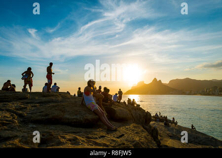 Silhouetten von Besuchern und Einheimischen Publikum auf den Felsen am Arpoador den Sonnenuntergang Blick auf Ipanema Beach in Rio de Janeiro, Brasilien zu genießen Stockfoto