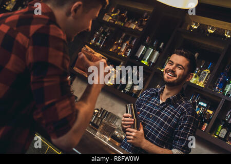 Junge Barkeeper stehen an der Theke holding Shaker im Gespräch mit Kunden fröhliche Stockfoto