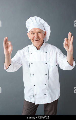 Senior Chef Studio stehen auf Grau lächelt Fröhlich angezeigt ok Zeichen isoliert Stockfoto