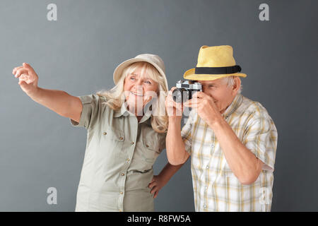 Ältere Touristen in Strand hüte Studio stehen isoliert auf Grau holding Kamera Fotos heiter Stockfoto