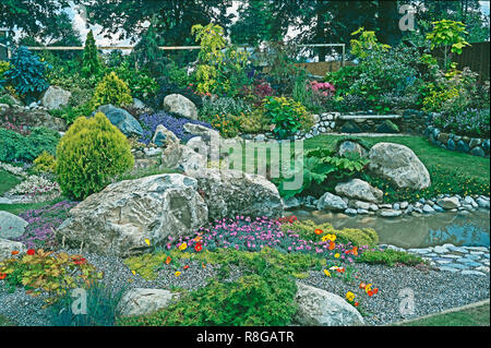 Steingarten und Wasser Garten mit gemischten Bepflanzung des alpinen Blumen, Pflanzen und Sträucher. Stockfoto