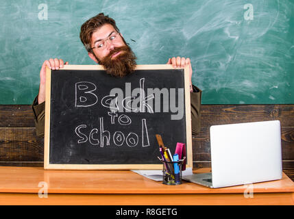 Zu Beginn des neuen Schuljahres im September. Lehrer oder Schulleiter begrüßt mit blackboard Inschrift zurück in die Schule. Willkommen zurück. Lehrer begrüßt neue Schülerinnen und Schüler der Bildungseinrichtung eingeben. Stockfoto