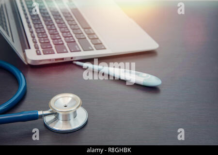 Blau Stethoskop und Thermometer und Labtop auf Holztisch, medizinisches Konzept Stockfoto