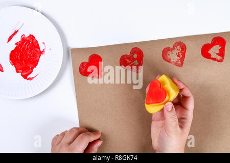 Diy. Geschenkverpackung für Valentinstag. Kraftpapier Geschenk und Kartoffel Stempel in der Form Herz und roter Farbe tun es sich am 14. Februar. Ansicht von oben o Stockfoto