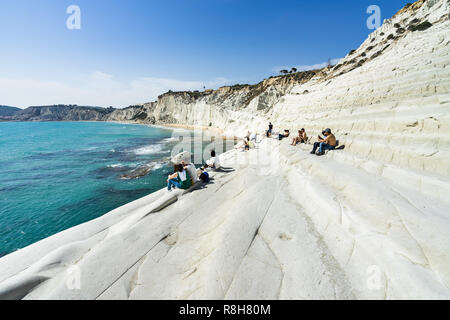 Touristen genießen die Sonne und das Meer auf den weißen Klippen von Scala dei Turchi (Treppe der Türken), Realmonte, Provinz Agrigento, Sizilien, Italien sitzen Stockfoto