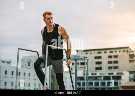 Mann in Fitness Kleidung zu Fuß die Treppen hinauf auf einem Dach weg schauen. Muskulösen Mann mit einem springseil an seinem Hals, Klettern auf dem Dach für fitn Stockfoto