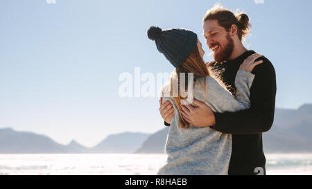 Liebespaar am Strand einander umarmen mit dem Meer im Hintergrund. Paar genießen am Strand an einem sonnigen Tag. Stockfoto