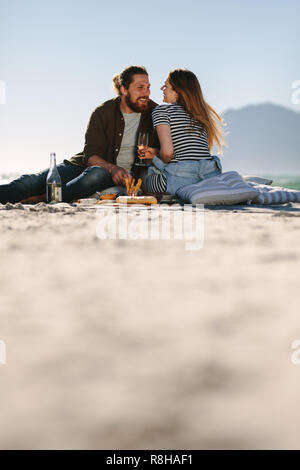 Schönes Paar genießen in einer guten Stimmung und Picknick am Strand. Low Angle View von Mann und Frau sitzen am Strand mit Speisen und Getränken. Stockfoto