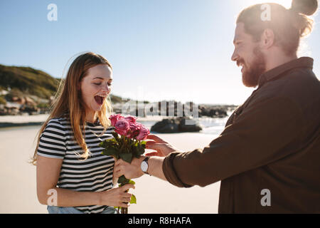 Freund überraschend Freundin mit Blumen am Strand. Mann überraschend Frau mit Bündel Rosen auf ein romantisches Date. Stockfoto