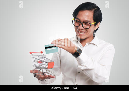 Foto Bild Portrait einer Lustig junge asiatische Geschäftsmann auf der Suche glücklich und lächelnd, während sie eine Kreditkarte in einem kleinen Einkaufswagen, Nahaufnahme Stockfoto