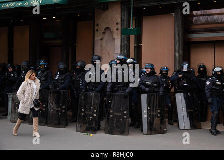 Paris, Frankreich, 15. Dezember, 2018. Lady Walking und Gruppe von Polizisten vor Café de la Paix, ein Café in der Nähe der Oper am Place de l'Opéra. Wie viele andere Restaurants und Geschäfte im Zentrum von Paris, das Café wurde geschlossen und abgesperrt mit Holzzäunen von Vandalismus zu verhindern. Rund 2.000 Demonstranten in gelben Westen ('Gilets Jaunes') demonstrierten in Paris gegen Steuererhöhungen und Kaufkraft Verluste für den fünften Samstag in einer Reihe. Credit: Christelle Chanut/Alamy leben Nachrichten Stockfoto