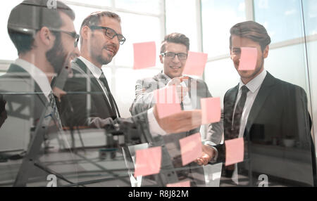 Kollegen lesen Haftnotizen auf Glas Stockfoto