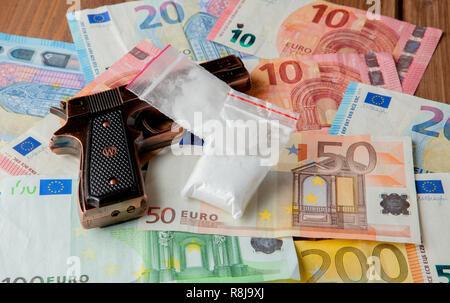 Schwarze Pistole und Pakete von Drogen vor dem Hintergrund der Euro auf einem Holztisch. Stockfoto