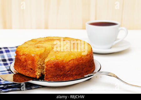 Hausgemachte Ananas Nach oben Torte mit einem Stück abschneiden und Tasse Tee auf weiße Holztisch Stockfoto