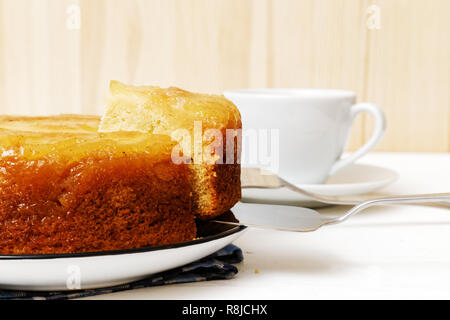 Hausgemachte Ananas Nach oben Torte mit einem Stück abschneiden und Tasse Tee auf weiße Holztisch. Flache konzentrieren. Stockfoto
