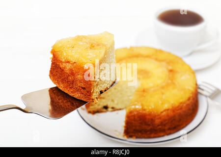 Hausgemachte Ananas Nach oben Torte mit einem Stück abschneiden und Tasse Tee auf weiße Holztisch. Flache konzentrieren. Stockfoto