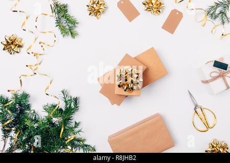 Stapel von geschenkboxen unter Festliche flach Zusammensetzung von Weihnachten goldene Verzierungen und Tannenzweigen auf weißem Hintergrund, Ansicht von oben. Stockfoto