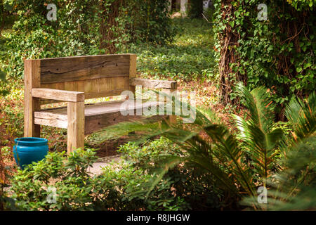 Eine Holzbank von Planken, die Risse haben und durch Zeit und Wetter verdunkelt. Bank steht in einem Park unter Bäumen Stockfoto