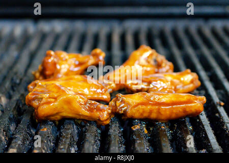 Glasierte Hühnerflügel auf einem Restaurant Grill. Nahaufnahme mit Grill Gitter vertikale. Stockfoto