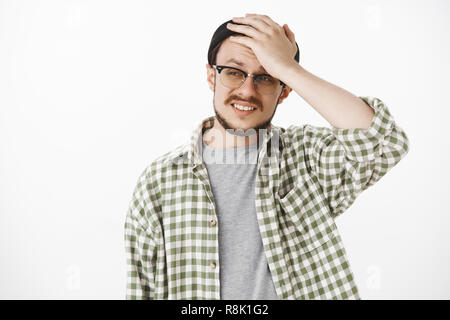 Taille - geschossen von cocnerned und unruhigen umgekippt Kerl mit Bart und Schnurrbart in Schwarz hipster Mütze und Brille, die Hand auf den Kopf und die Stirn runzelnd frimacing stucking in schwierigen und verwirrenden Situation Stockfoto