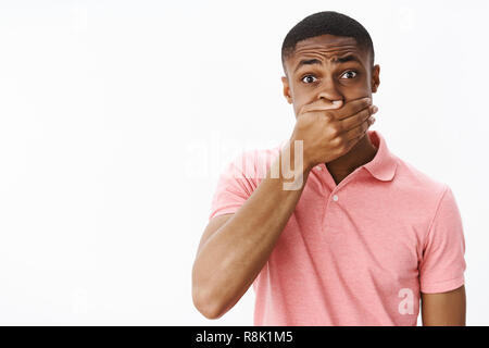 Studio shot der nervösen afrikanischen amerikanischen männlichen Freund Leid und betäubt rutscht Geheimnis unpurposely schlagen sich mit Palm auf Mund geschockt suchen und an der Kamera über graue Wand verwirrt Stockfoto