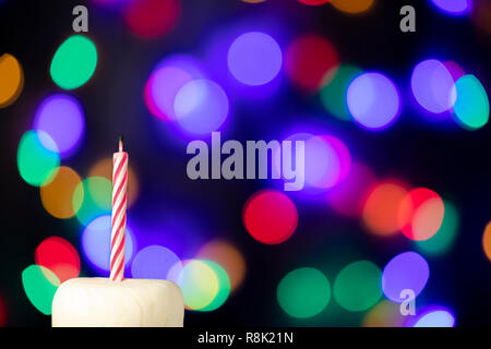 Geburtstag Kerze auf einem weißen Kuchen mit bunten Lichtern im Hintergrund Stockfoto