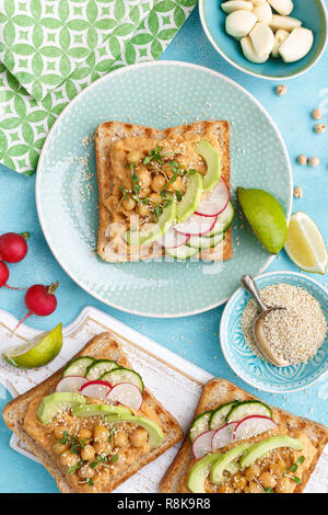 Toast mit Kichererbsen Hummus, Avocado, frische Radieschen, Gurken, Sesam und Leinsamen Sprossen. Diät Frühstück. Leckere und gesunde pflanzliche Veg Stockfoto