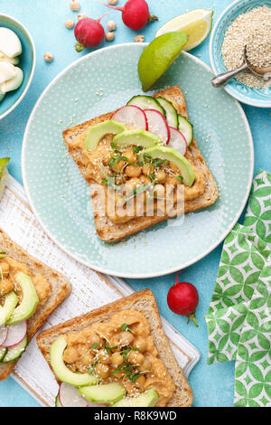 Toast mit Kichererbsen Hummus, Avocado, frische Radieschen, Gurken, Sesam und Leinsamen Sprossen. Diät Frühstück. Leckere und gesunde pflanzliche Veg Stockfoto