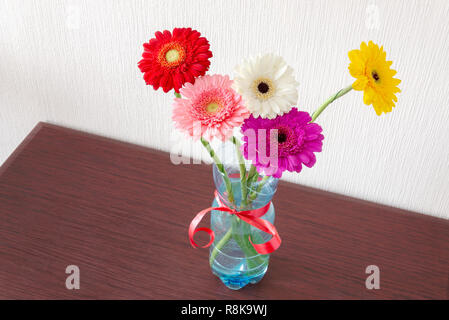 Fünf bunten Gerbera Blumen in einem plasctic Trinkflasche mit einem roten Band, auf einem Holztisch Stockfoto