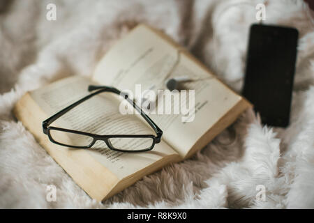 Ein altes Buch auf Decke Decke mit Horn - eingefaßte Brillen und ein Handy mit Headset, eine friedliche Szene Stockfoto