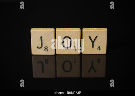 WOODBRIDGE, NEW JERSEY, November 9, 2018: Scrabble Tiles, buchstabieren Sie das Wort Freude an einem reflektierenden schwarzen Hintergrund Stockfoto