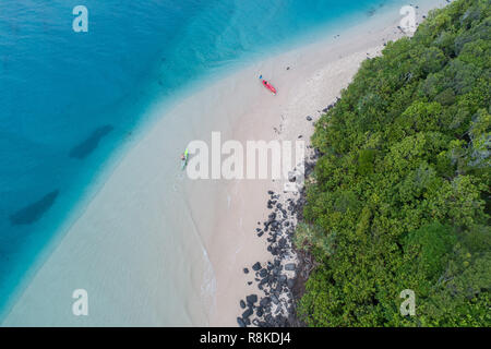 Mann Kajak in einem blauen Ozean in der Nähe von einem tropischen Strand ideal für Fitness, Spaß, Angeln und Urlaub. Luftaufnahme bei Sonnenaufgang. Stockfoto