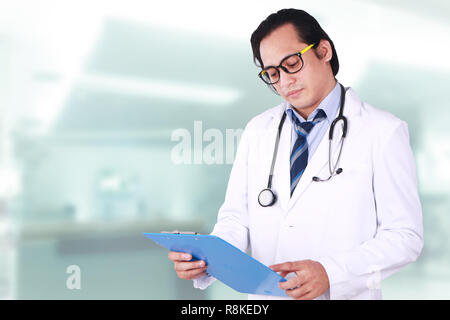 Foto Bild portrait einer jungen asiatischen männlicher Arzt mit Brille, Blick nach unten, lesen zu seinen Patienten Anmerkungen Stockfoto