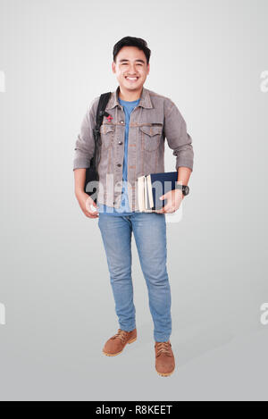 Foto Bild Portrait einer netten jungen asiatischen männliche Kursteilnehmer stehen, zu Kamera suchen und lächelnd, während Sie einige Bücher, voller Körper portrait Stockfoto